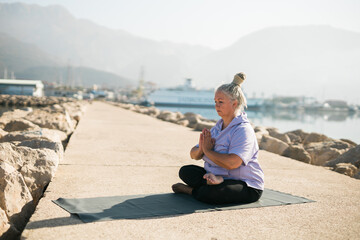 Fototapeta na wymiar Mindful senior woman with dreadlocks meditating by the sea and beach copy space - wellness and yoga practice