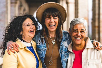 Multiracial senior women having fun together outdoor at city street- three happy mature trendy female friends hugging and laughing on urban place- Friendship lifestyle concept with elderly people  - Powered by Adobe