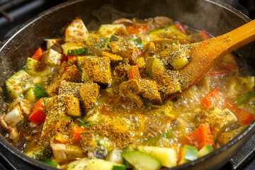 A frying pan with stewed vegetables and a wooden spoon on the stove .