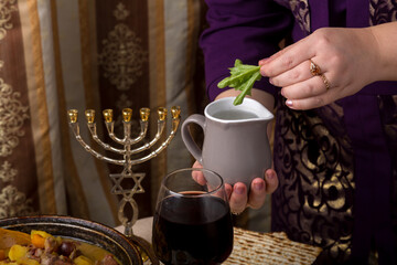 A woman at a table set for a Passover seder dunks bitter herbs into a jar of salt water.