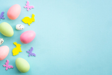 Easter background on blue. Eggs, rabbit, spring flowers and butterfly. Flat lay with copy space.