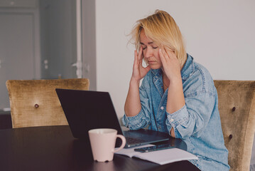 Stressed woman working from home on laptop looking worried, overwhelmed. Exhausted female working...