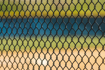 a fence background with a softball/baseball field in background.