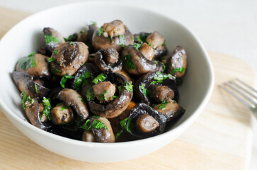 Fried champignons with garlic and parsley in a gray bowl. Vegetarian lifestyle concept. Horizontal orientation. Selective focus.
