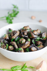 Fried champignons with garlic and parsley in a gray bowl. The concept of vegetarian food. Vertical orientation. Selective focus.