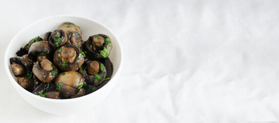 Fried champignons with garlic and parsley in a white bowl. The concept of vegetarian food. Horizontal orientation. Selective focus. Banner. Copy space.