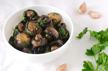 Fried champignons with garlic and parsley in a white bow with ingredients on the table. Vegetarian lifestyle concept. Horizontal orientation. Selective focus.