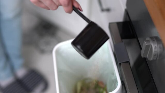 Person pouring bokashi ferment in a compost container in the kitchen. Female recycling organic food leftovers in a composter bin with fermenting bran at home