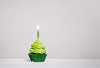 Green cupcake with sprinkles and lit birthday candle on a white grey background. - 588462164