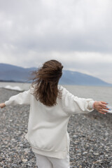 Fototapeta na wymiar girl with her back against the background of the sea and mountains in a white suit