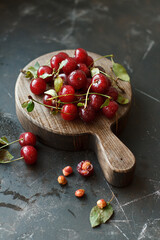 Fresh ripe cherries on wooden cutting board over dark concrete background. Side view, copy space