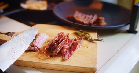 Close up chef cutting slicing roasted juicy freshly grilled meat beef steak with fork and knife on wooden cutting board at the kitchen