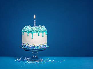 White birthday drip cake with teal ganache and lit candle over dark blue background - 588463516