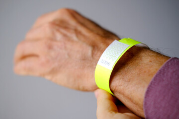 close-up of neon yellow paper bracelet on the male arm of adult clinic patient, check tape with...