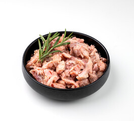 Canned pork or chicken stew in a black bowl with rosemary on a white isolated background.