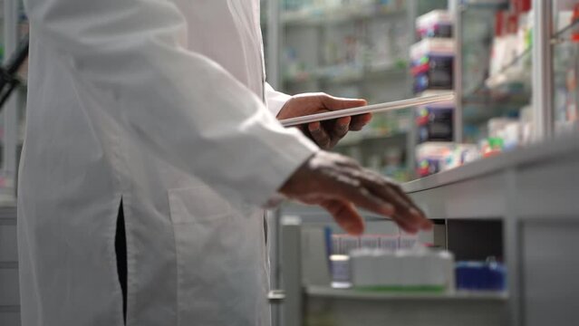Get a glimpse of the efficient workflow in a retail drugstore as a male black pharmacist uses a digital tablet PC to assemble online medication orders for delivery. 4K high-quality footage