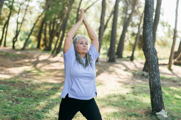 Senior woman with dreadlocks in stretching position on nature at morning. Elderly woman doing yoga on park - wellbeing and wellness tai chi