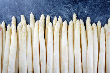 Roher weißer Spargel mit einer Reihe als close-up mit Textfreiraum oben auf grauem Hintergrund