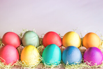 Vibrant colorful easter eggs in a basket on a light pink background