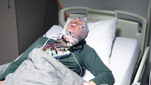 Middle aged woman measuring brain waves, examining polysomnography in sleep lab