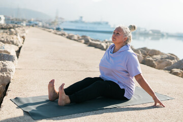 Fototapeta premium Mature old woman with dreadlocks practicing yoga and tai chi outdoors by the sea - wellbeing and wellness