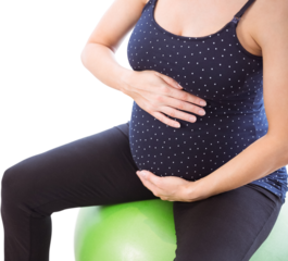 Pregnant woman holding belly while sitting on exercise ball