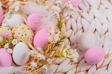 Obraz na płótnie Canvas Easter candy chocolate eggs and almond sweets lying in a bird's nest decorated with flowers and feathers on white background. Happy Easter concept.