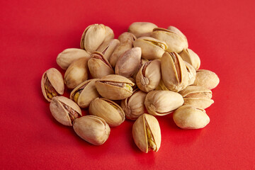 A pile of pistachios with shells on a red background.