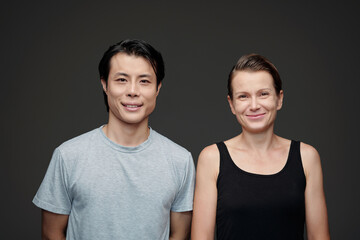 Obraz premium Portrait of smiling diverse couple standing against gray background and looking at camera