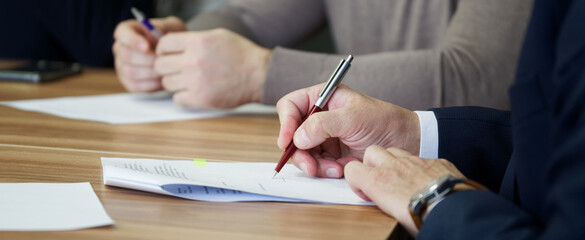Hands of an adult man with a fountain pen signing a document, agreement or memorandum during a...