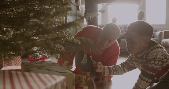 Mother and son looking at Christmas tree decorations with multi generational family celebrating