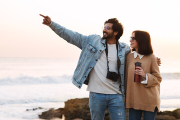Cheerful young indian man and caucasian woman in casual and glasses with thermos enjoy travel