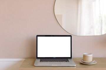 Laptop with blank screen mockup, ceramics on wood console table, modern mirror on the beige wall. Branding, portfolio, graphic design template.