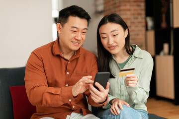 Family shopping online. Korean husband and wife using cellphone and credit card, making payment in store via smartphone