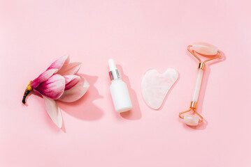Rose quartz crystal facial roller and gua sha scraper, face serum or organic cosmetic oil on pink background. Facial massage kit for lifting therapy . Skin care anti-aging tools. Top view, flat lay