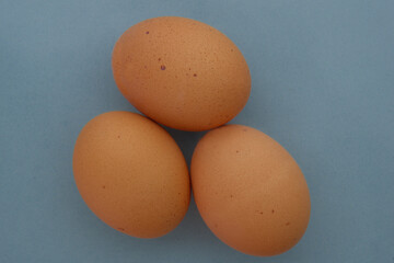 Top down view of three brown speckled chicken eggs on a blue background concept organic, free range