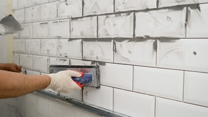 White tile in the kitchen with gray grout. The process of applying grout to ceramic tiles. Small ceramic tiles. Black grout for white ceramic tiles.
