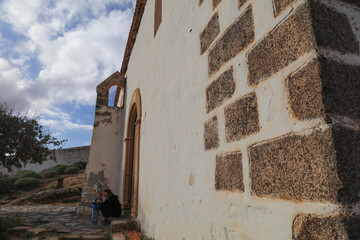 Fuerteventura, Canary island, Spain - Jan 22, 2023: typical medieval Spanish building from canary island with tourist family seating out. Side facade of a monastery with wood balcony.