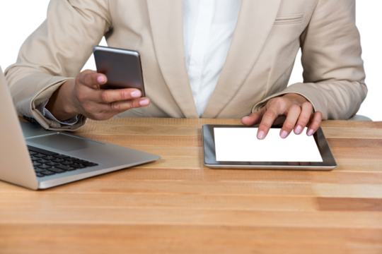 Midsection of Businesswoman using mobile phone and digital tablet with laptop on table