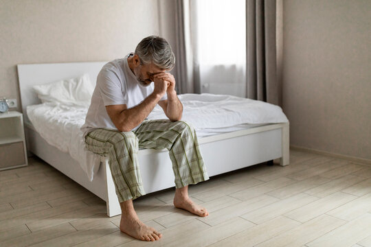 Depressed grey-haired mature man sitting on bed in the morning - Powered by Adobe