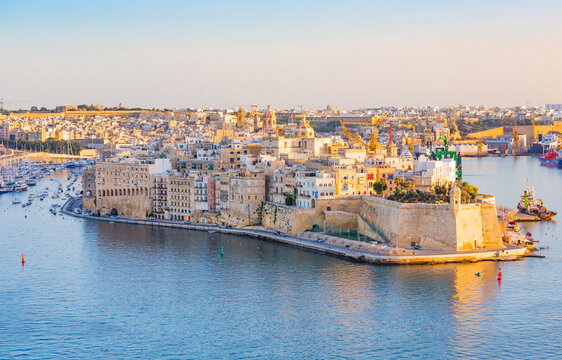This stunning photograph captures the three historic cities of Malta - Vittoriosa, Senglea, and Cospicua - basking in the warm glow of a golden sunset. Taken from the vantage point of La Valeta, the c
