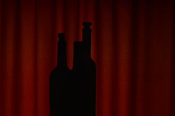 Silhouettes of bottles against dark red curtains in evening light