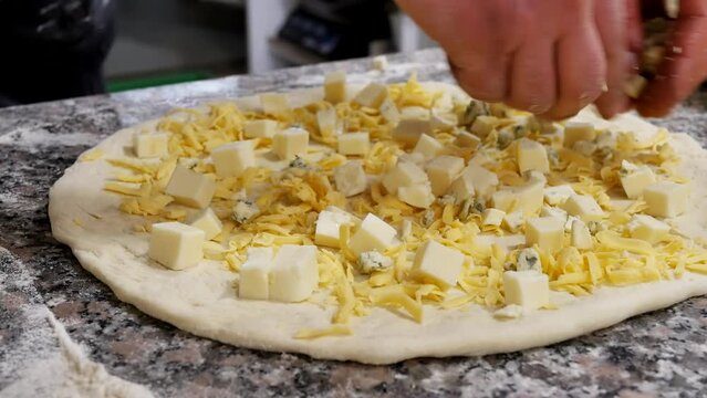 The hands of the chef pour slices of cheese with dorblu mold onto the pizza, adding mozzarella and grated Swiss cheese to it. cooking pizza from different types of cheese. traditional italian food
