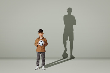 Happy caucasian 6 years old little kid in casual with soccer ball and shadow of adult soccer player