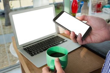Cropped hands of designer using phone by laptop