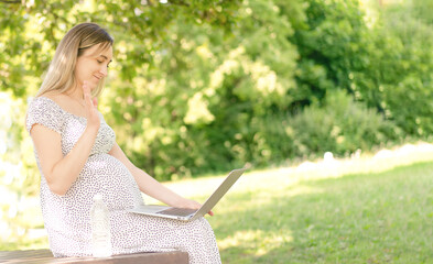 A pregnant woman communicates with friends via a computer in the park.