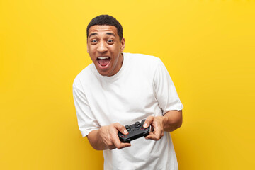 joyful guy african american gamer holds joystick and plays video game on yellow isolated...