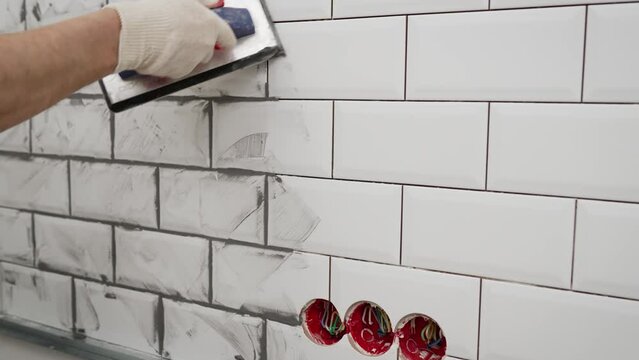 Grouting white tiles. Grouting tiles with rubber trowel man hand. Professional worker gluing decorative tile on wall.