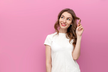 young pensive woman in white t-shirt dreams and thinks on pink isolated background, the girl...