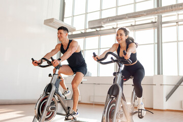 athletic couple of cyclists train on static bicycle simulator, man trainer and fitness woman go in for sports together